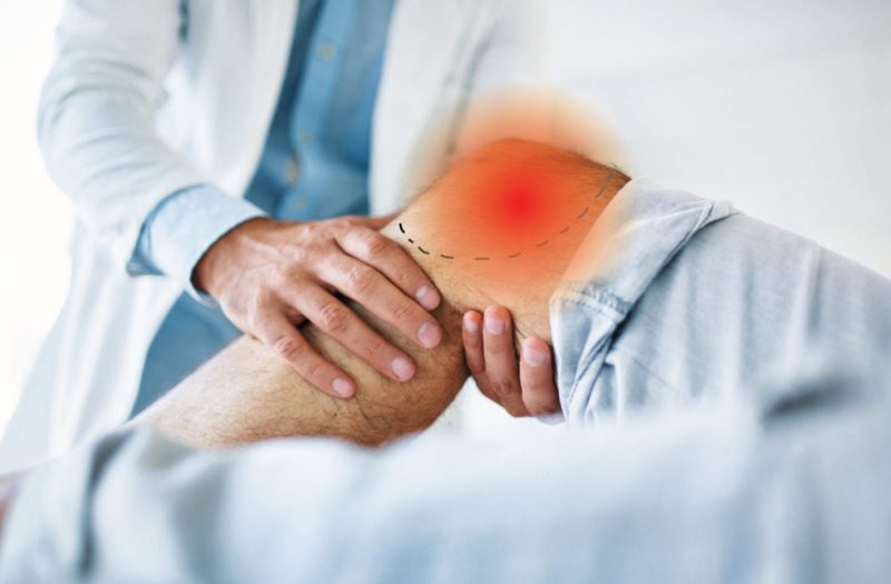 A doctor evaluating a person's knee, which is inflicted with knee osteoarthritis, as evident by a red pain spot.