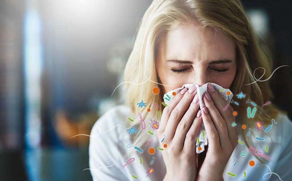 Image shows a photo of a woman sneezing and cartoon germs spraying from her mouth and nose