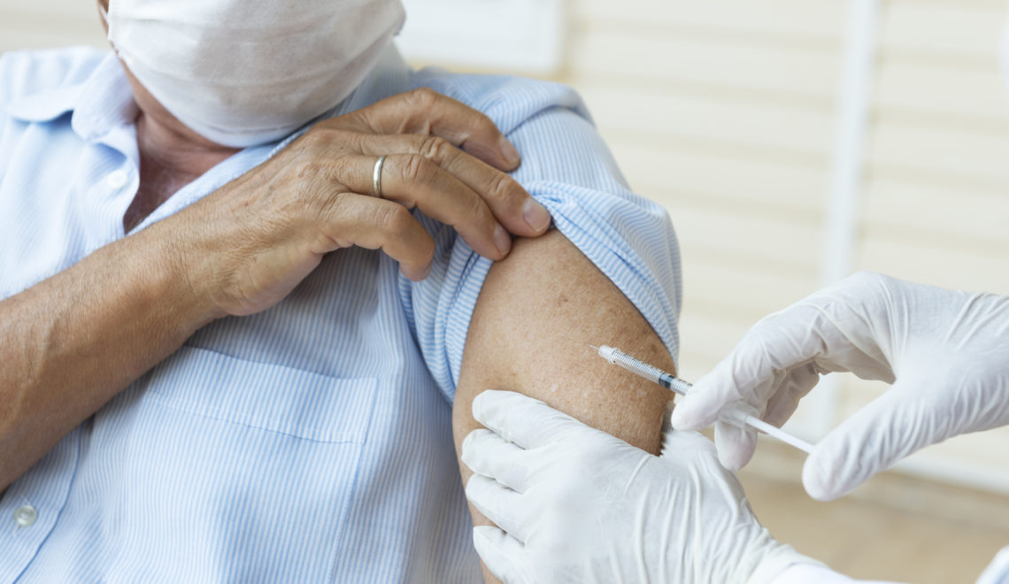 Senior man wearing a protective face mask is getting vaccination from a person with white surgical gloves.