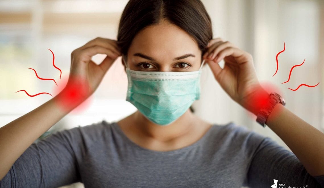 Photo of a latina woman wearing a face mask. There are red spots on her wrists indicating joint pain