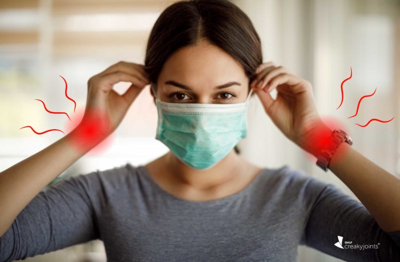 Photo of a latina woman wearing a face mask. There are red spots on her wrists indicating joint pain