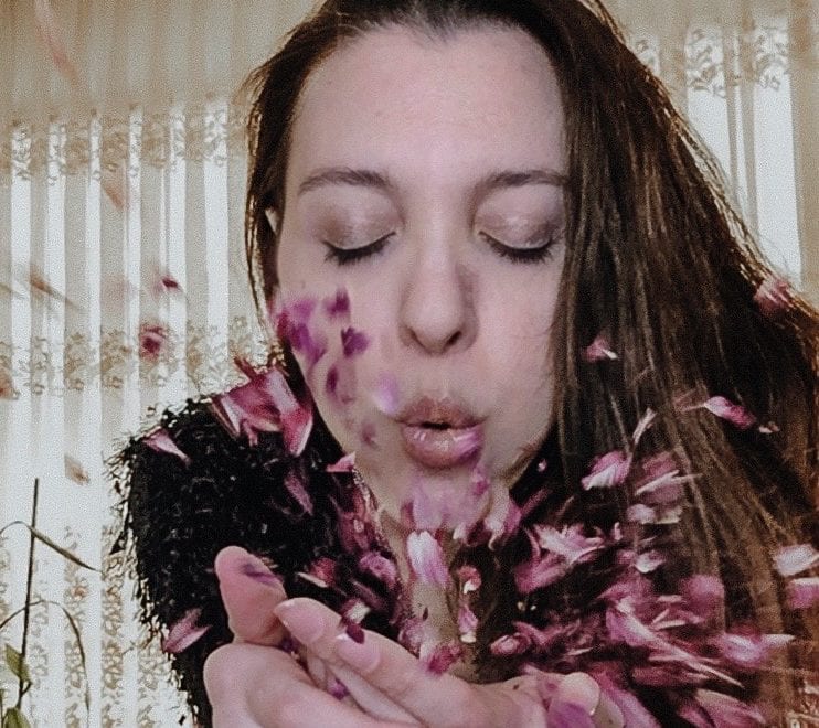 Photo fo a woman blowing petals from her hands into the camera