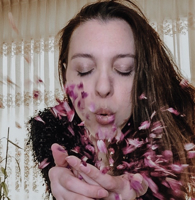 Photo fo a woman blowing petals from her hands into the camera