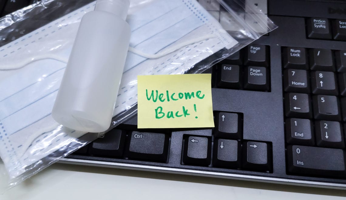 Welcome note with hand sanitizer and mask on work keyboard; Back to work note with alcohol gel to prevent coronavirus / infection