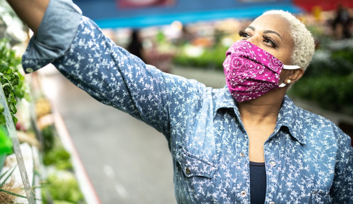 A photo of a Black woman grocery shopping while wearing a face mask.