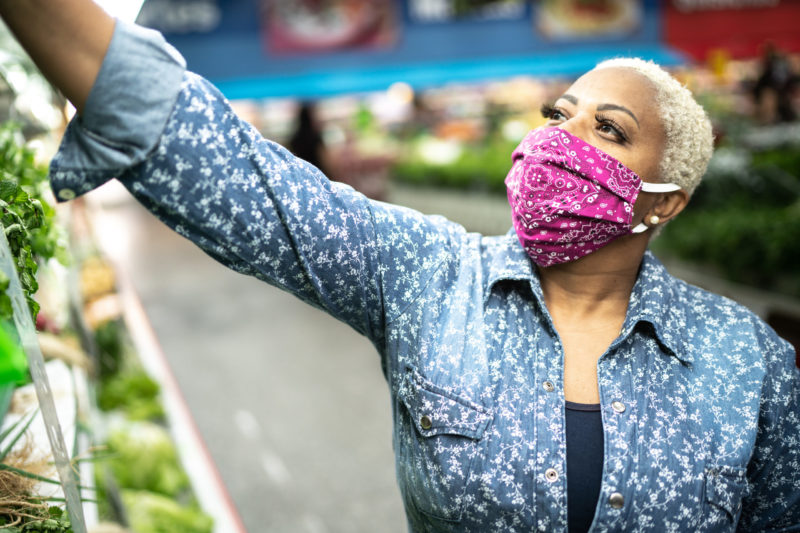 A photo of a Black woman grocery shopping while wearing a face mask.