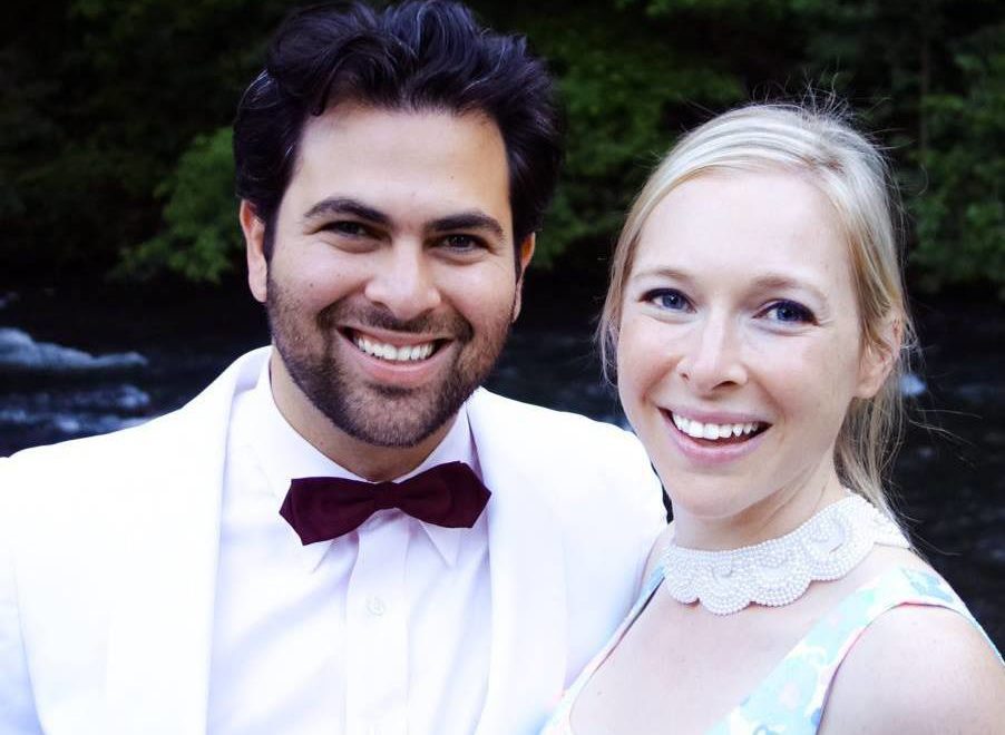 A photo of a man, Seth Ginsberg, wearing a white tuxedo and a woman, Cara Zelas wearing a printed dress.