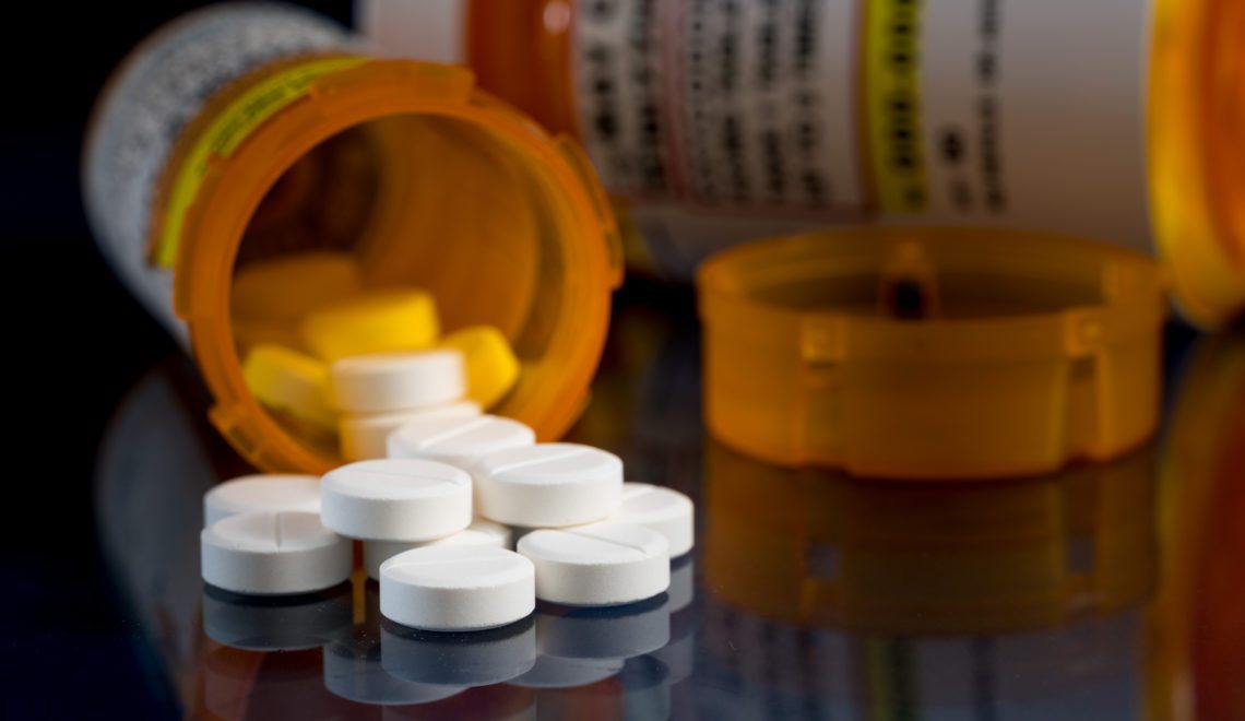 A photo of a bottle of oxycodone, a type of opioid. The bottle is laying on a table with small, white circular tablets falling out of it.