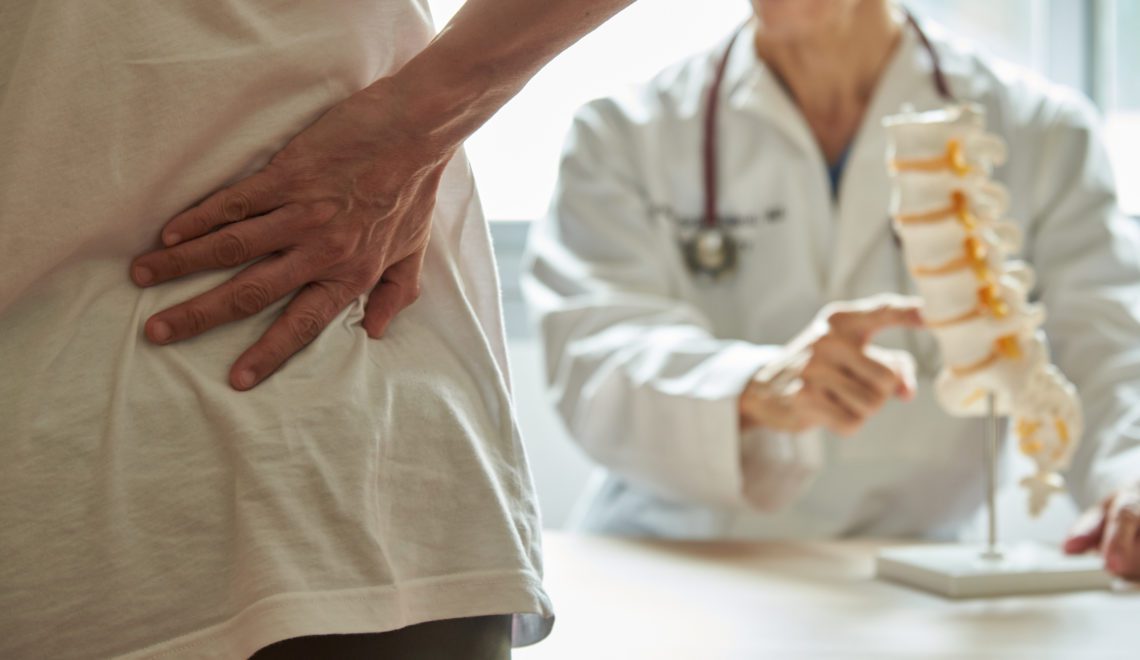 A male doctor explaining lumbar anatomy to female patient complaining of back pain at medical clinic