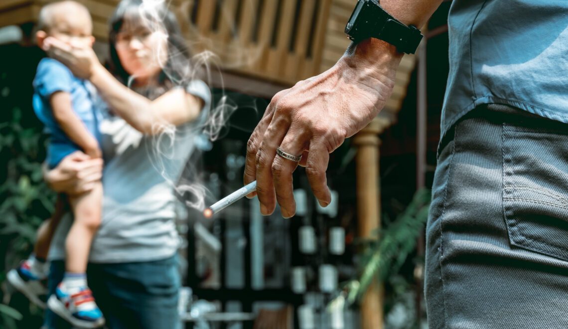 A photo of a mother carrying a child, scolding a father who is holding a cigarette.