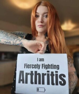 Image of woman holding a printed out sign that says 'fiercely fighting arthritis'