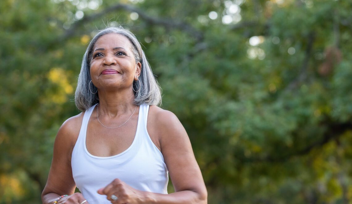 Photo of a Black senior citizen woman in a workout tank top going for a power walk in a park