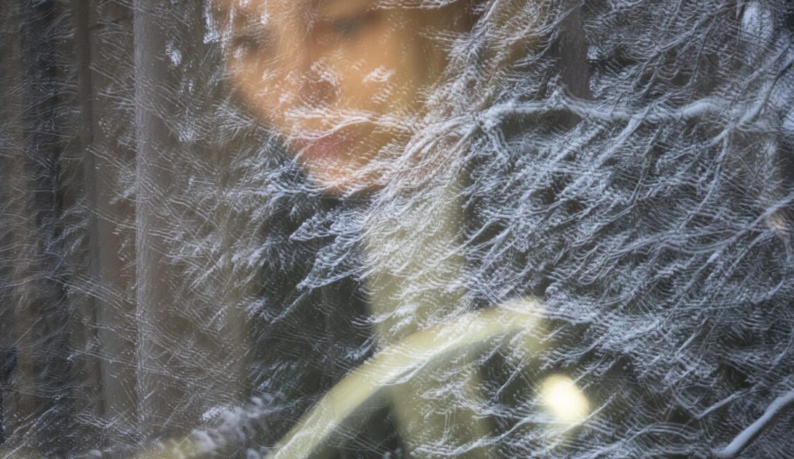 Photograph of a person sitting by a window with a snow-covered tree reflecting in the glass, to go with an article about coping with a chronic illness during winter