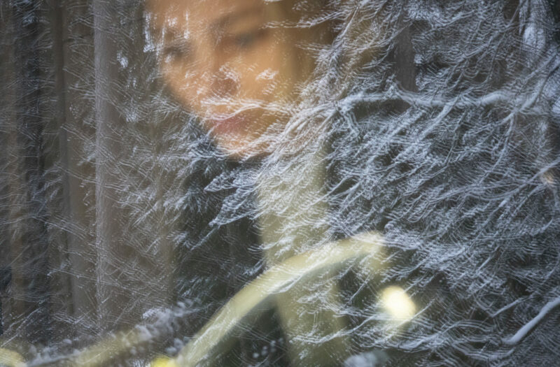 Photograph of a person sitting by a window with a snow-covered tree reflecting in the glass, to go with an article about coping with a chronic illness during winter